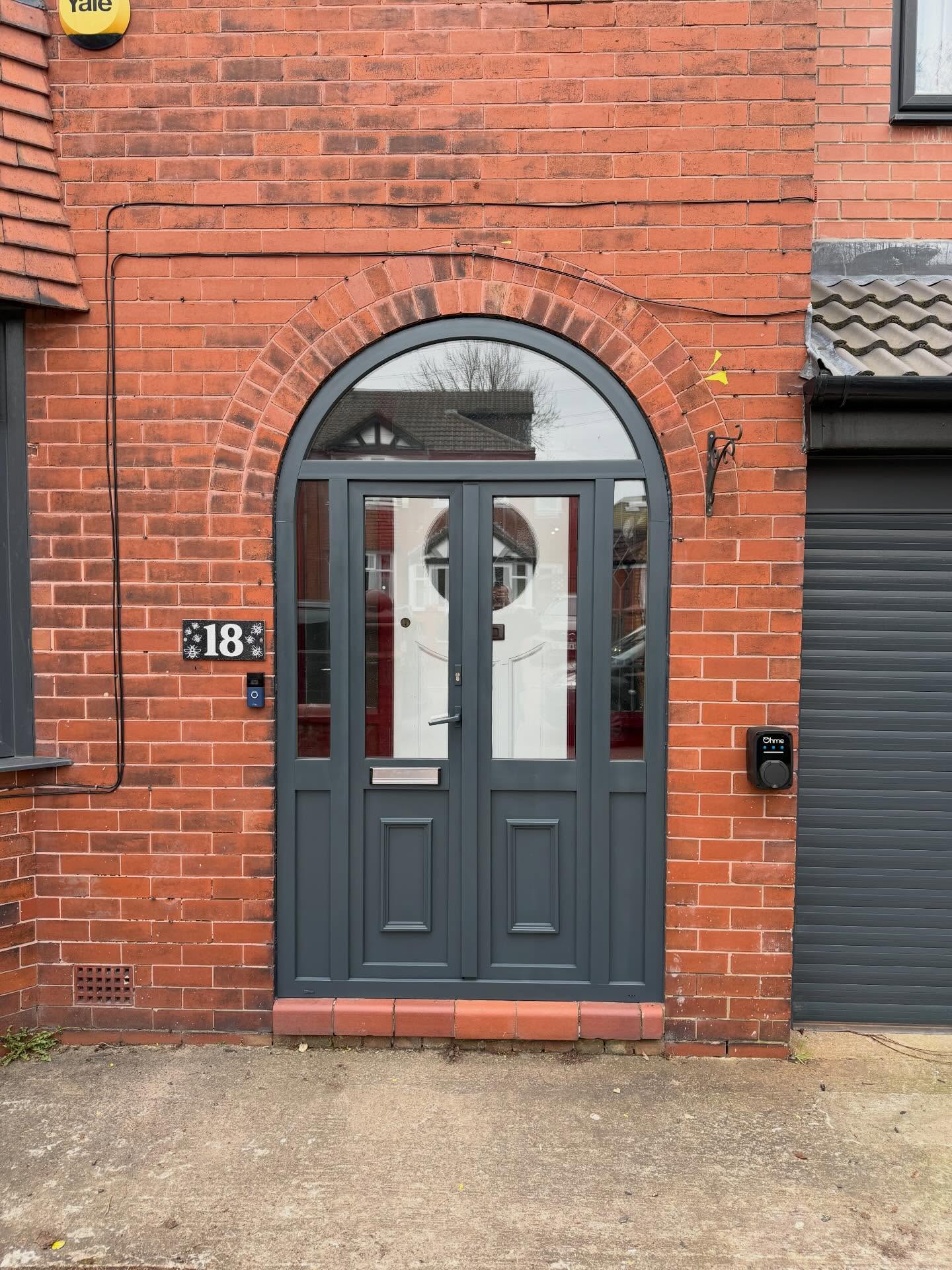 Arched uPVC front door and frame resprayed anthracite grey against red brickwork.