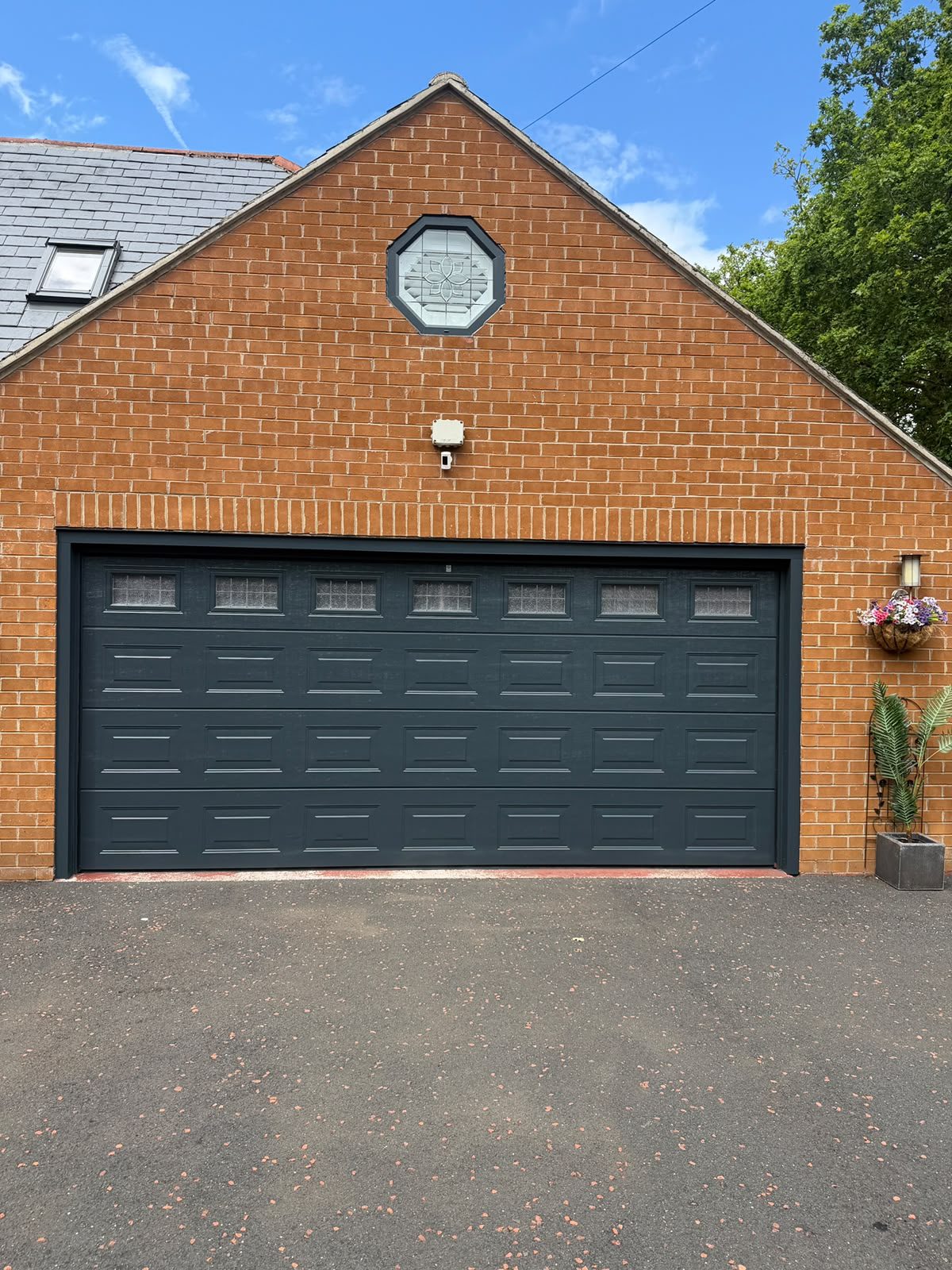 Double garage door and octagonal window resprayed anthracite grey against orange brickwork.