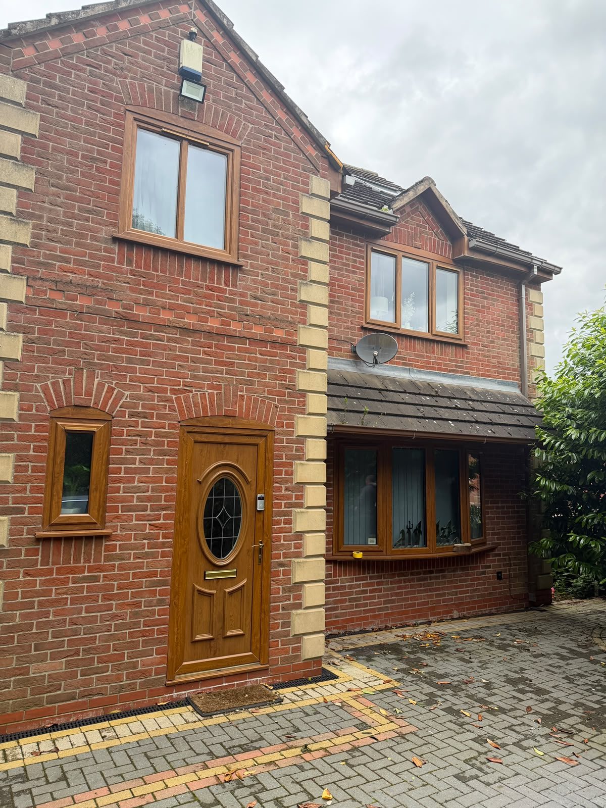 Golden oak uPVC front door, bay window and casement windows on a red brick house before spraying.